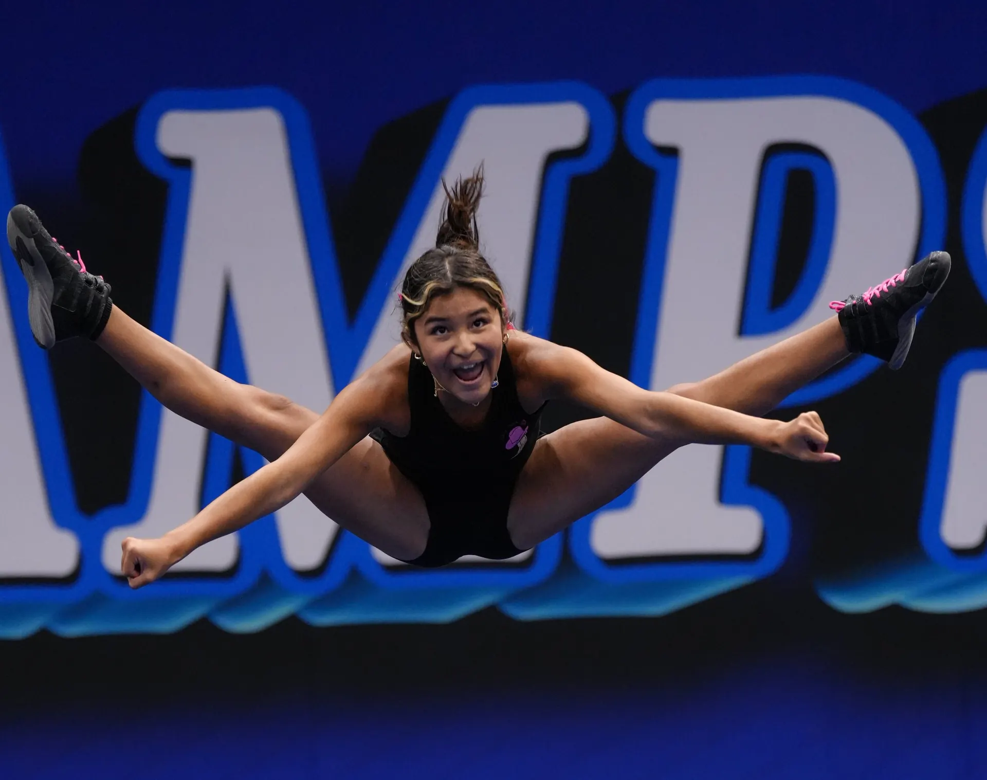 An athlete hitting a toe-touch in front of the Dream Camps letters
